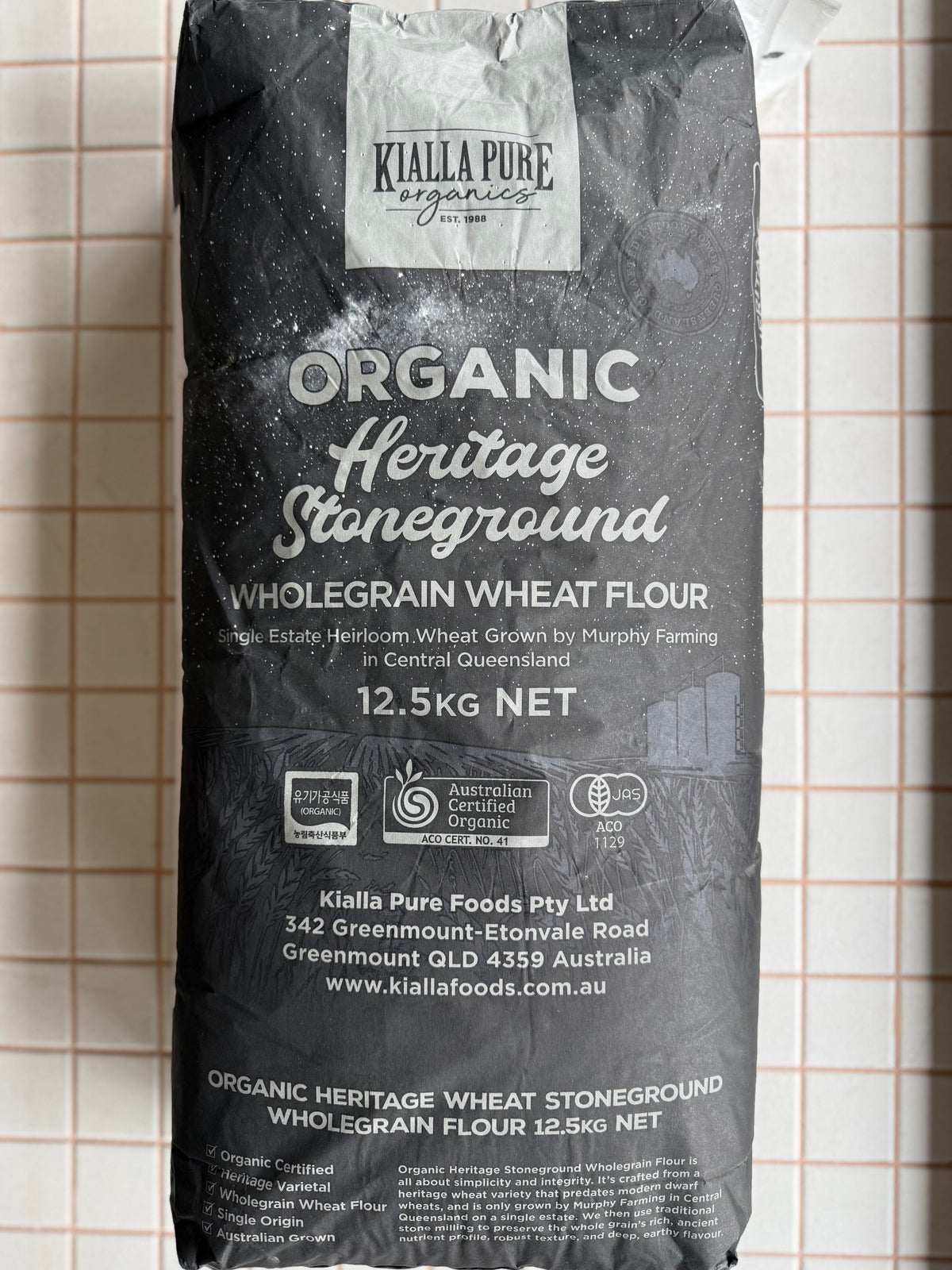 A 12.5kg bag of Kialla Pure Organics Organic Heritage Stoneground Wholegrain Wheat Flour, photographed against a white tiled background.