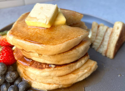 Stack of pancakes with butter and syrup on a plate with fruit.