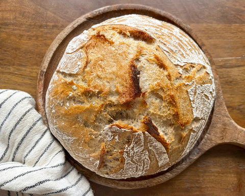 Loaf of bread on a wooden board with a striped towel.